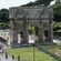 Turistas en una estructura enorme, antigua y cuadrada con 3 arcos amplios y altos tallados en ella